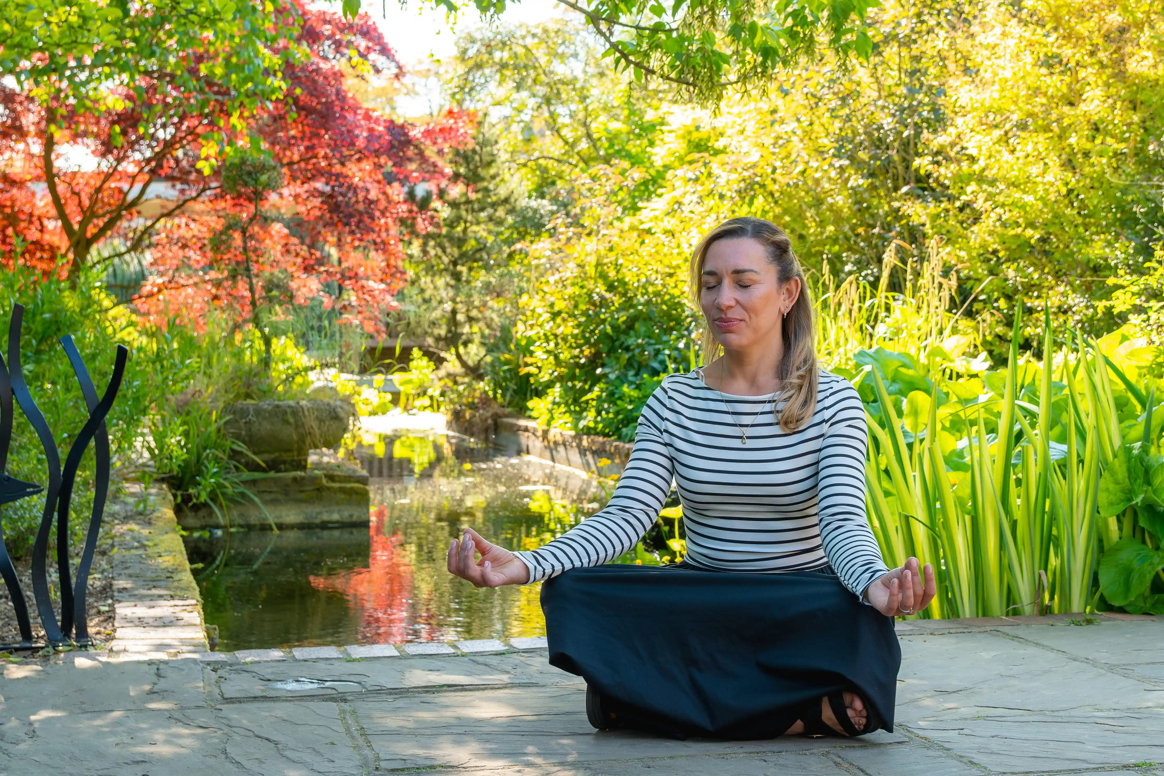 A woman sits on the ground in a colourful garden meditating